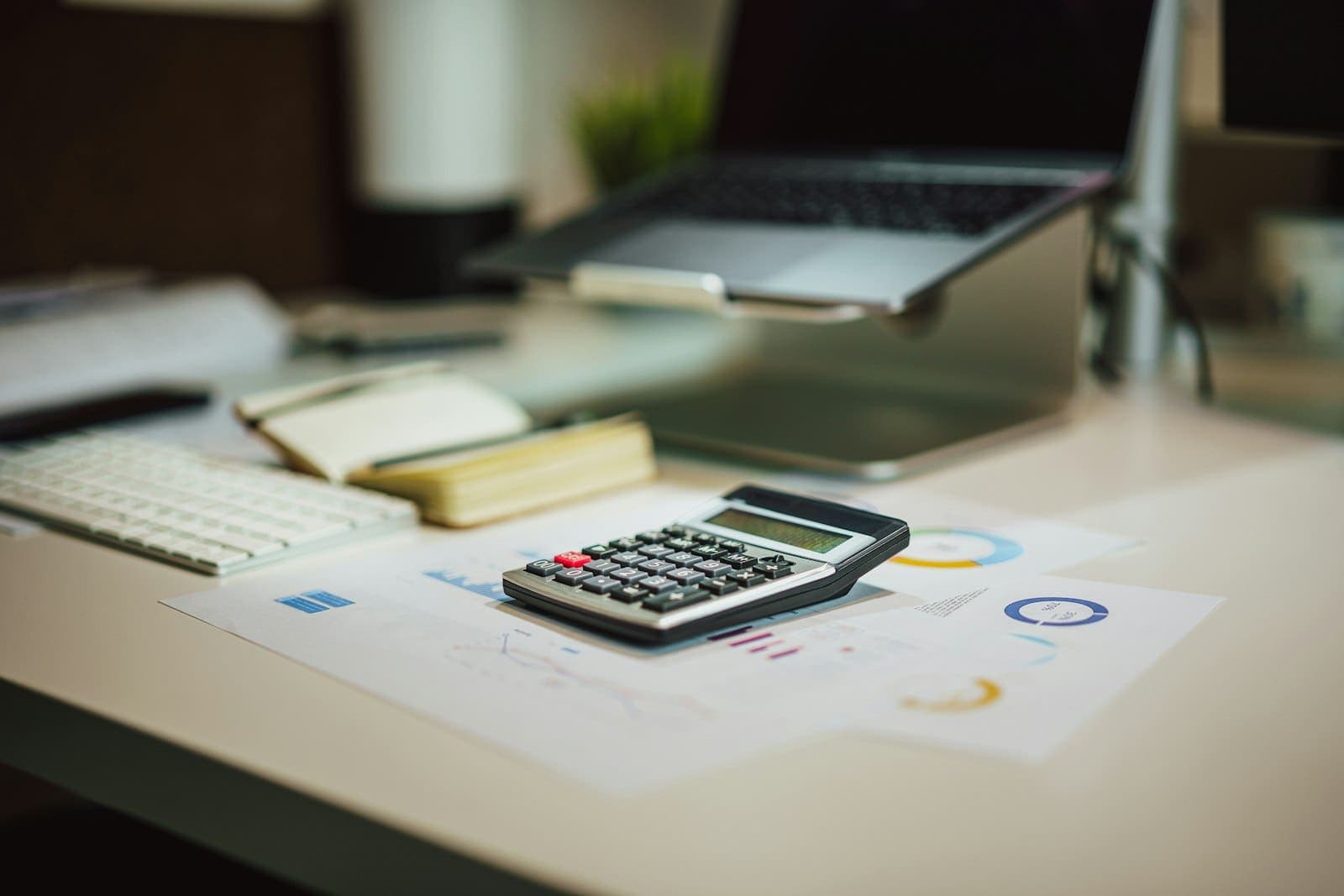 Mesa de trabalho com calculadora, notebook e relatórios impressos com gráficos de valores