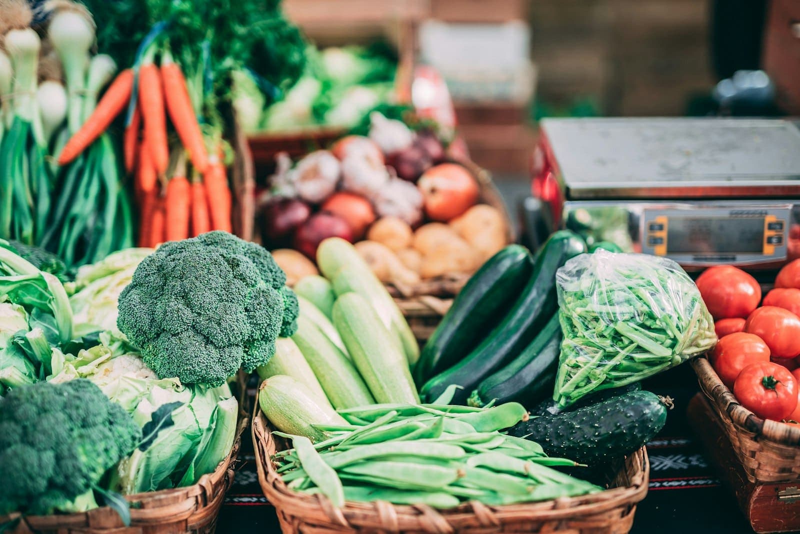 Brócolis, abobrinhas, vagens, cenouras e tomates em cestos de vime ao lado de uma balança