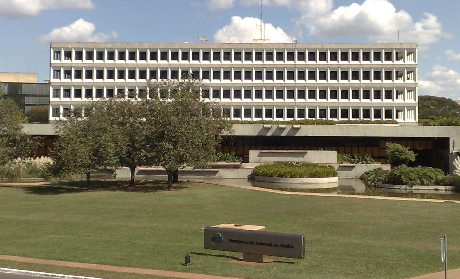 Prédio da sede do Tribunal de Contas da União em Brasília, com gramado e placa do tribunal à frente